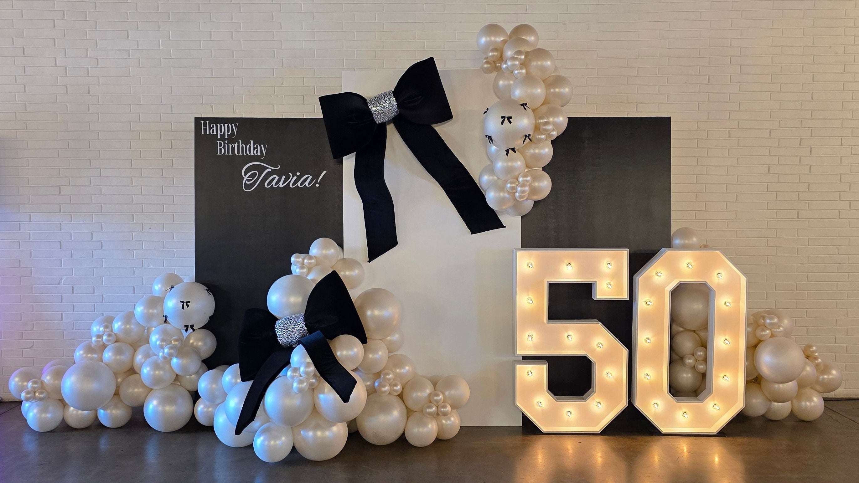 Decorative setup with '50' lights, pearls, and a card on a textured wall.