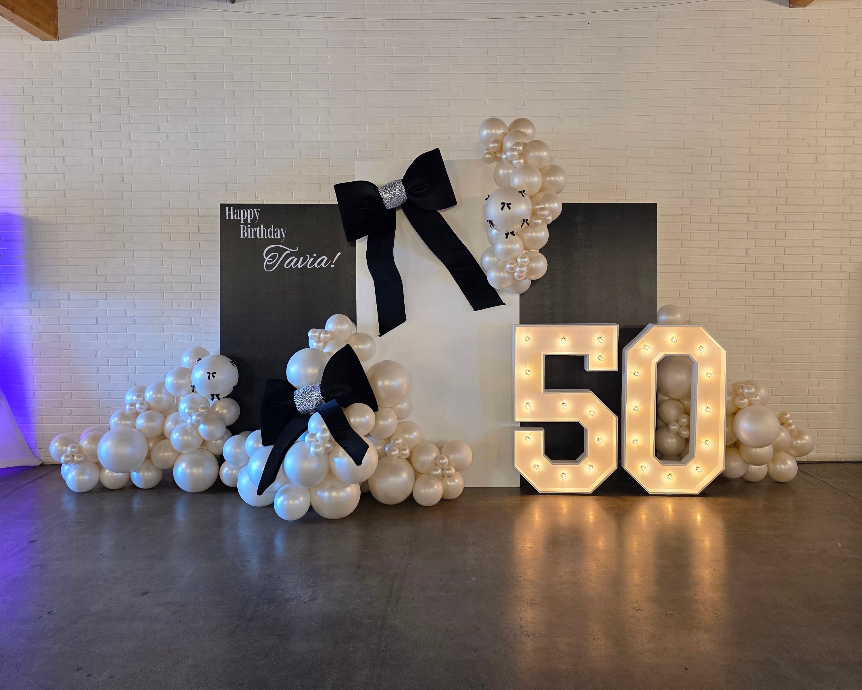 Decorative setup with '50' lights, pearls, and a card on a textured wall.