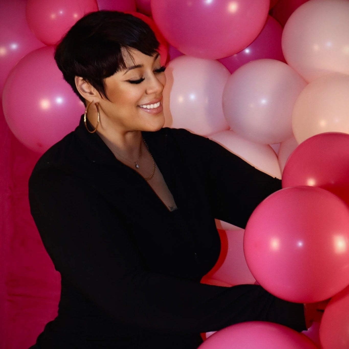 Woman in a black outfit surrounded by pink balloons