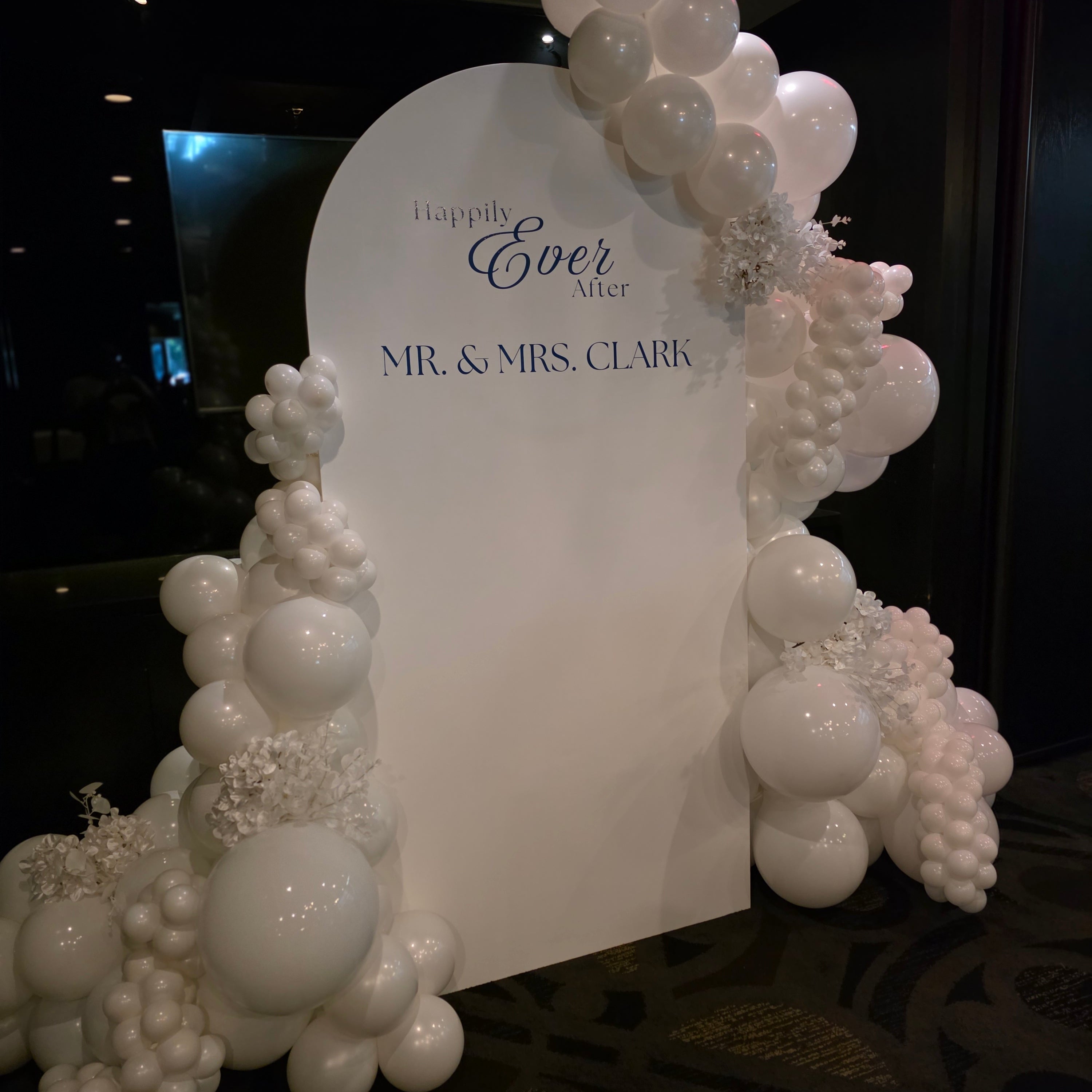 Decorative balloon arch with a white card in the center on a dark background